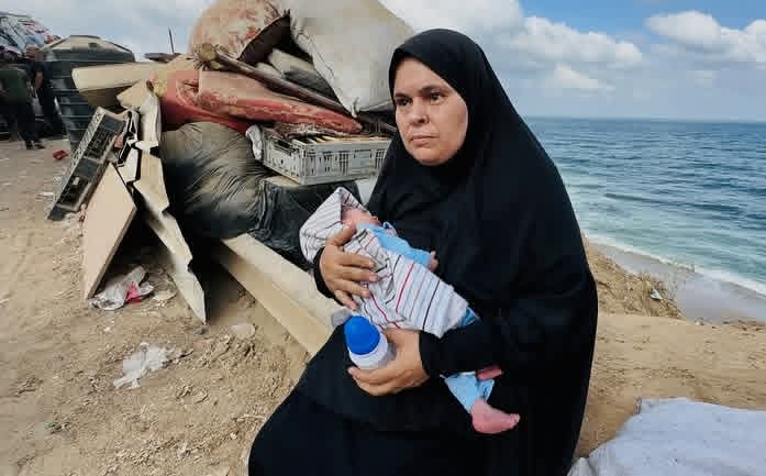 Woman carries infant amid displaced people with fear and hope