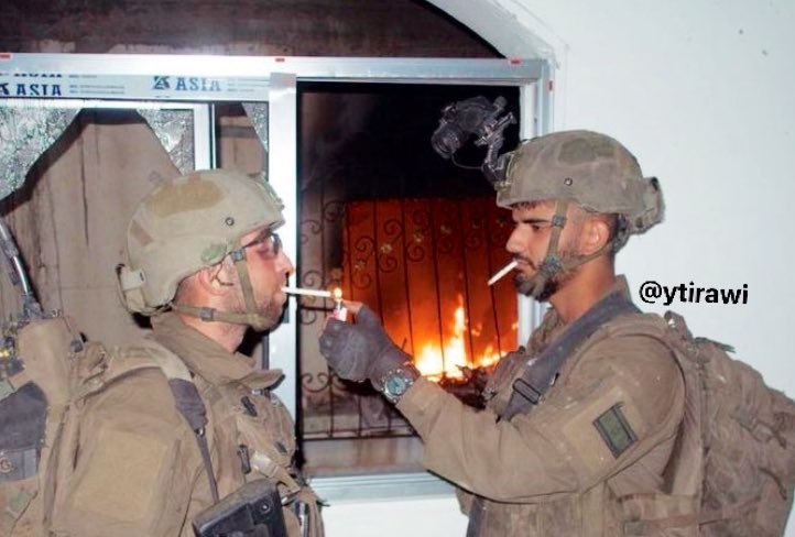 Israeli soldiers smoke while Palestinian house burns in Gaza