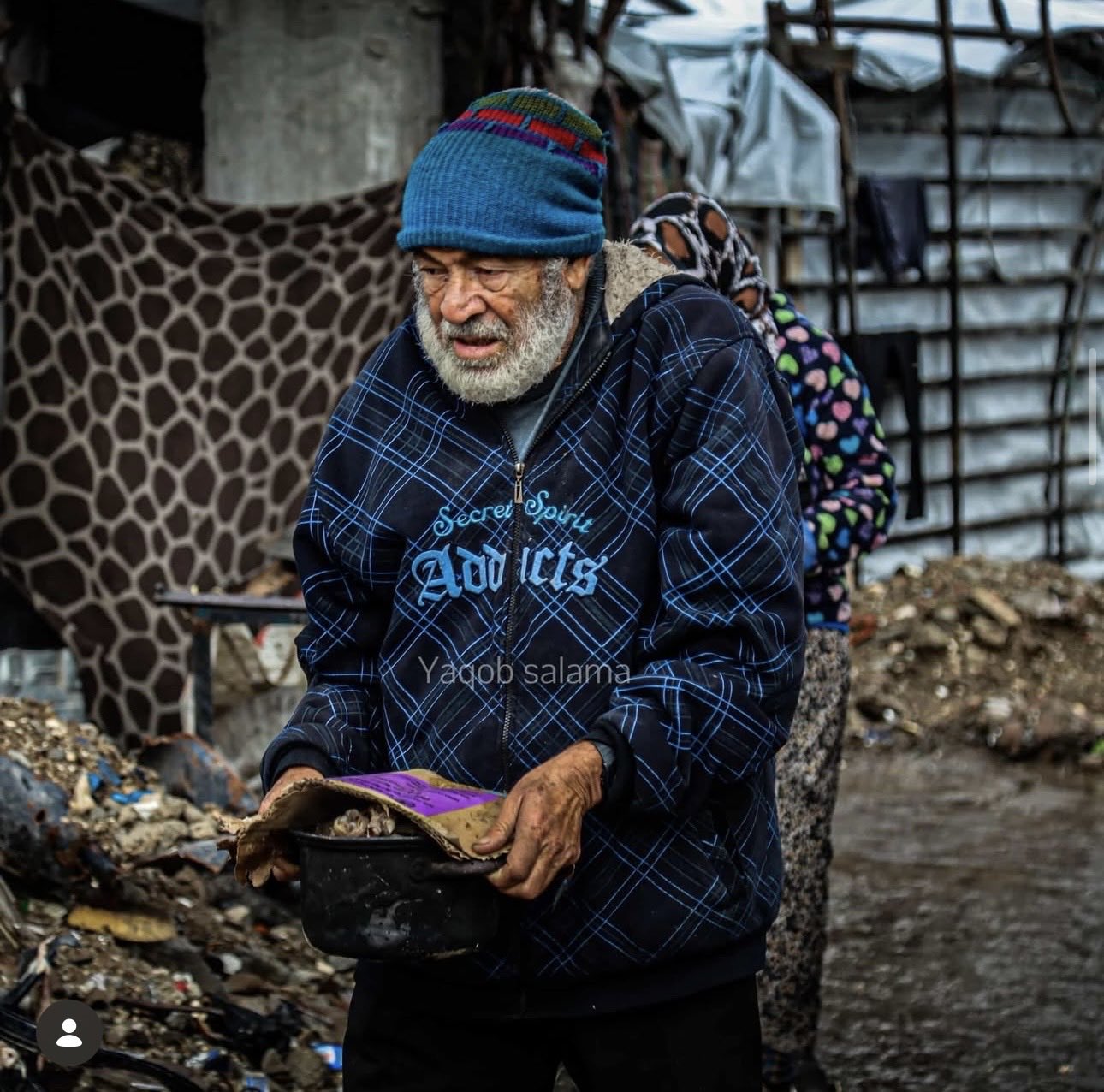 Elderly Palestinian shields his meal from rain to feed family