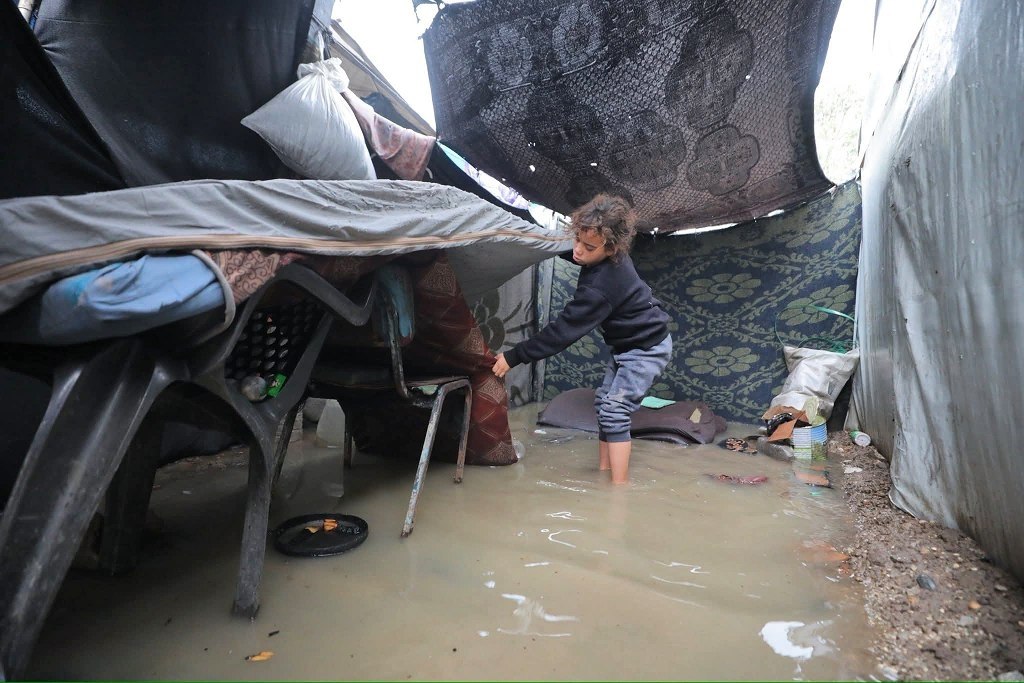 Girl Protects Family Belongings as Floodwaters Submerge Displacement Tent