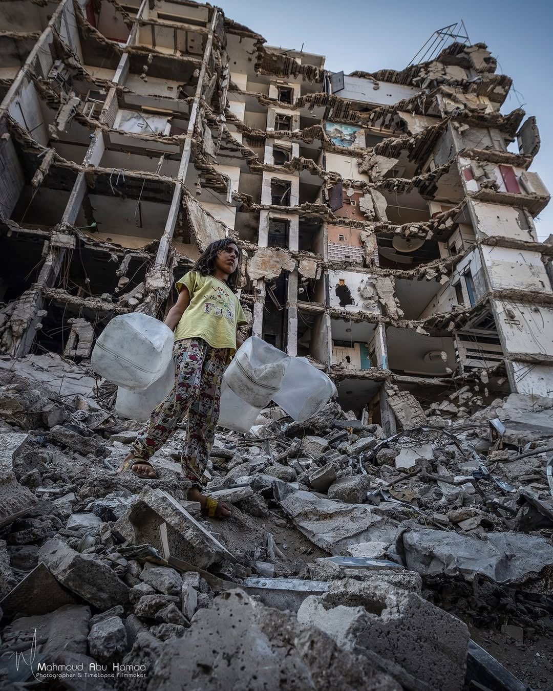 Child collects water amid rubble under blockade