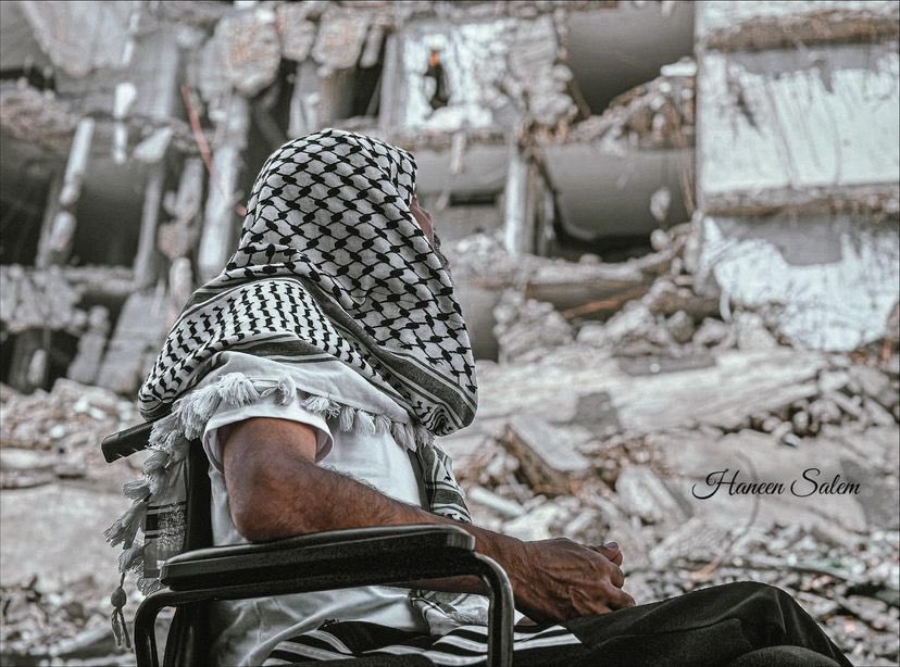 Man with amputated leg in rubble, wearing keffiyeh